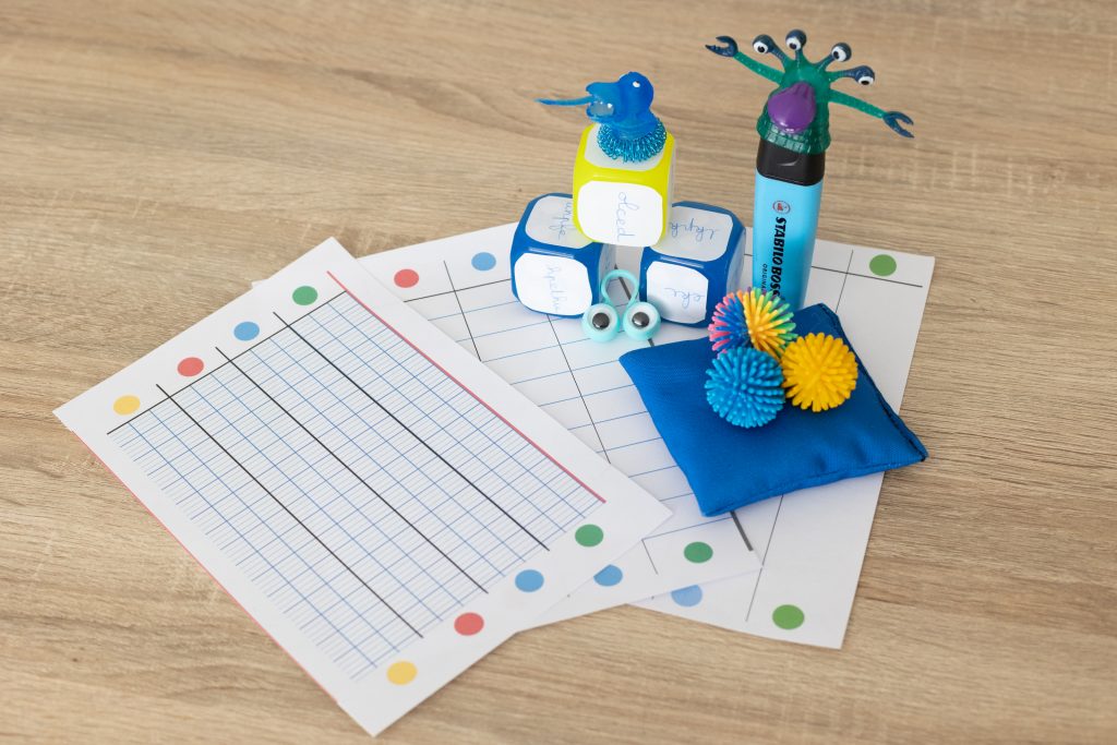 @clic_and_chlo – Traits de plume Outils ludiques et sensoriels pour aider les enfants à améliorer leur écriture : feuilles à grands carreaux colorés, dés avec mots, balles tactiles et accessoires pédagogiques.